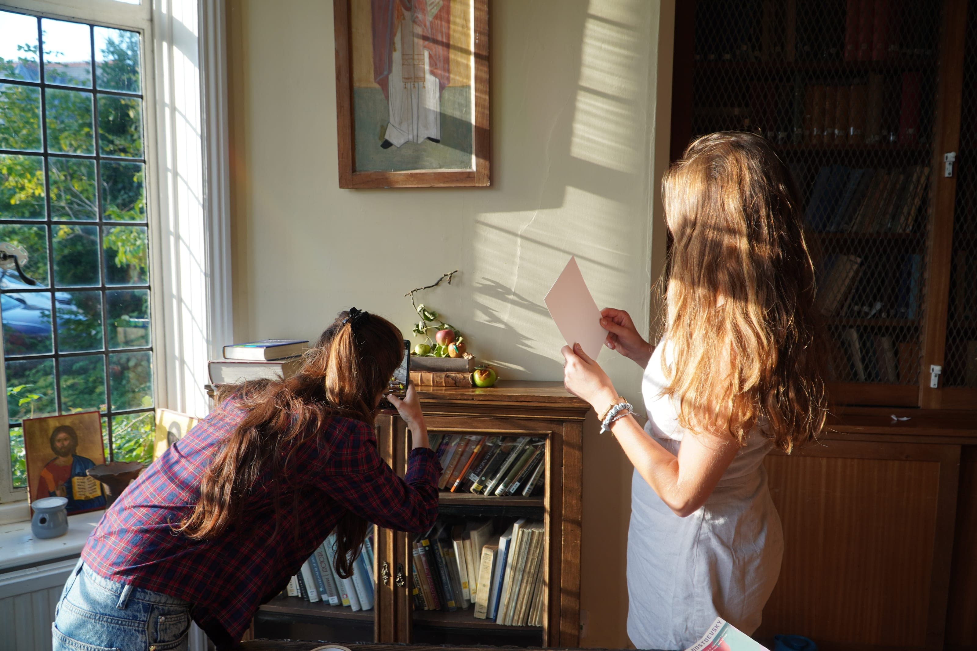Photographing a still life beside a sunlit window, one hand holding a card to bounce the light